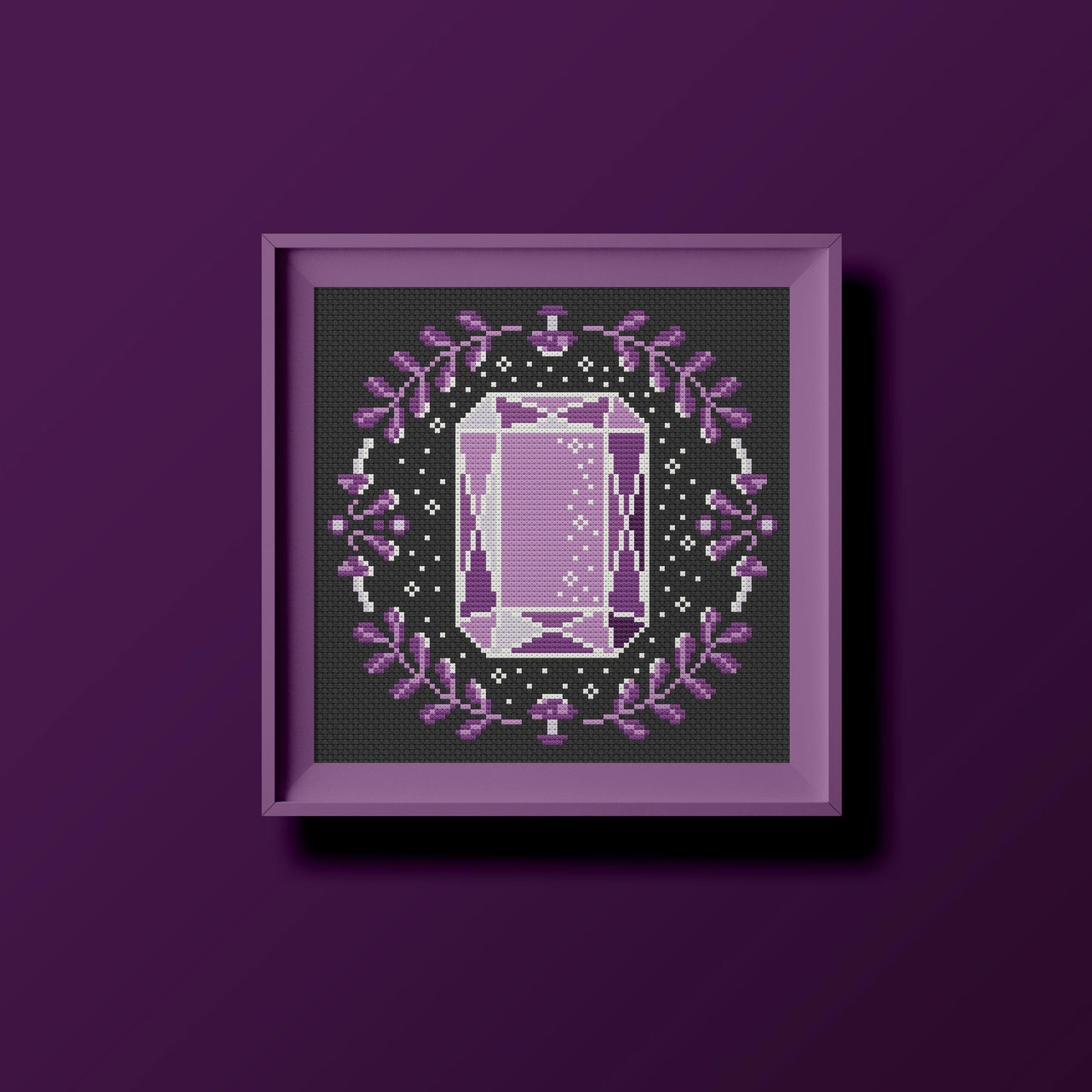Patrón de punto de cruz para bordar una gema de forma octagonal y color lila, rodeada de hojas, setas y estrellas. Punto de cruz moderno sobre tela negra.