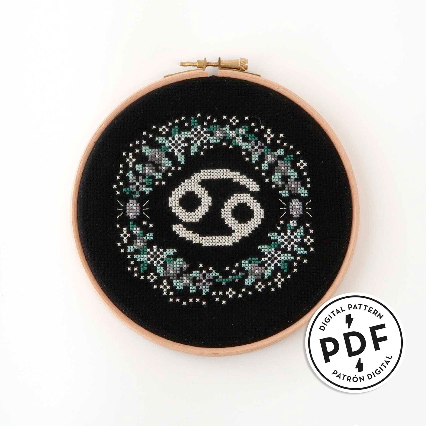 Patrón de punto de cruz en PDF con el signo de Cáncer rodeado de flores en tonos de gris. Signo del zodíaco de punto de cruz moderno y redondo para enmarcar en aro de bordar.