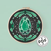 Esquema de punto de cruz en pdf "Joya Verde Esmeralda". Esquema de bordado de una gema de color verde en forma de lágrima rodeada de hojas, flores y estrellas. Punto de cruz moderno.