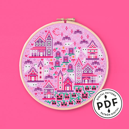 Esquema de punto de cruz de un pueblo con casitas de color rosa y lila, fantasmas, murciélagos lilas y calabazas rosas. De estilo gótico pastel.